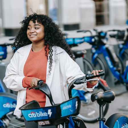 smiling black woman walking with bicycle along street renting station